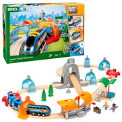BRIO Action Tunnel Travel Set tartalma a doboz mellett – motoros vonat, fa sínek, állomás, színes alagutak, fák, figurák és kiegészítők kreatív játékhoz.