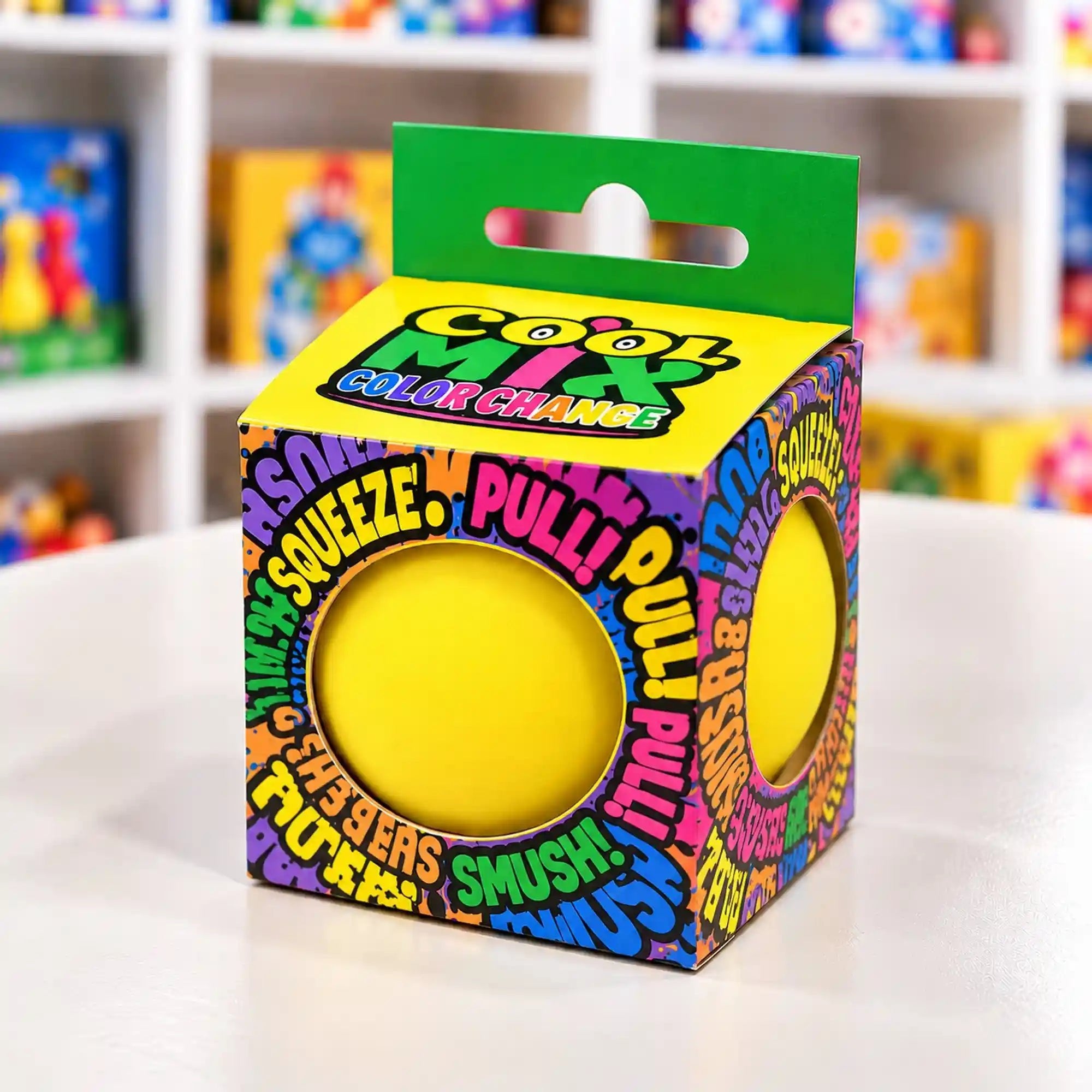 Cool Mix Squishy 7 cm stresszlevezető játék (sárga) – Élénksárga squishy labda színes, kör alakú kivágásokkal ellátott dobozban, játékbolti környezetben.