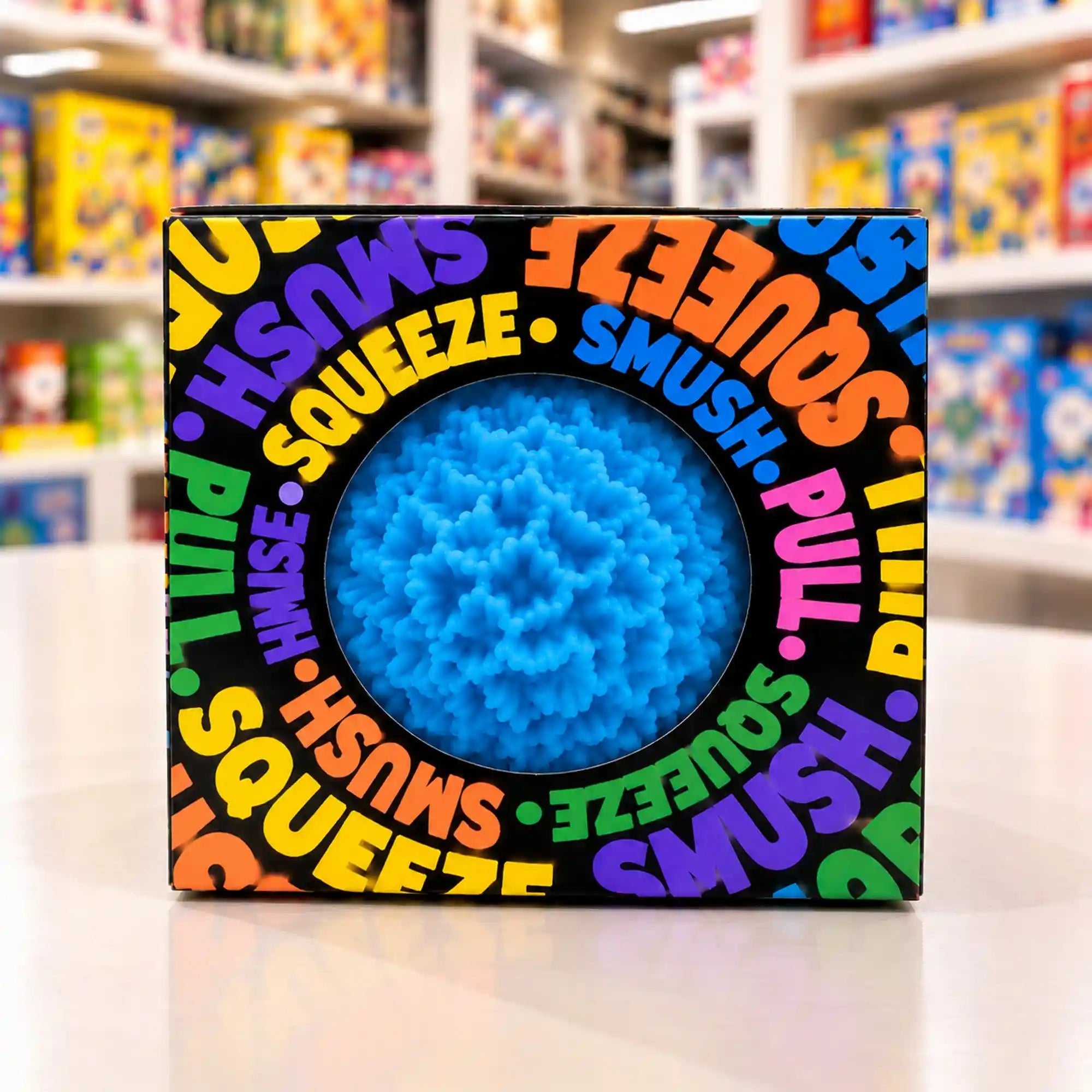Cool Mix Squishy: Bolyhos tapintású labda 6 cm stresszlevezető játék (kék), fekete, színes feliratokkal díszített dobozban, kör alakú ablakon keresztül látható.