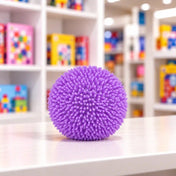 Cool Mix bolyhos tapintású squishy stresszlabda (lila) – lila színű, puha tüskékkel borított, gömb alakú stresszlabda fehér asztalon, elmosódott játékbolti háttérrel.