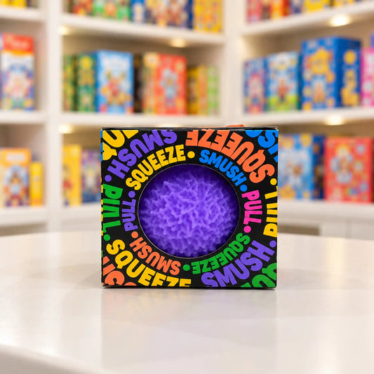 Cool Mix Squishy: Bolyhos tapintású labda 6 cm stresszlevezető játék (lila), fekete, színes feliratokkal díszített dobozban, kerek ablakon keresztül látható lila labdával.