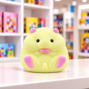 Cool Mix Squishy: Hörcsög stresszlevezető játék (sárga) – sárga, pufók hörcsögfigura rózsaszín fülekkel, mancsokkal és szájrésszel, fekete szemekkel, világos asztalon, elmosódott játékbolti háttér előtt.