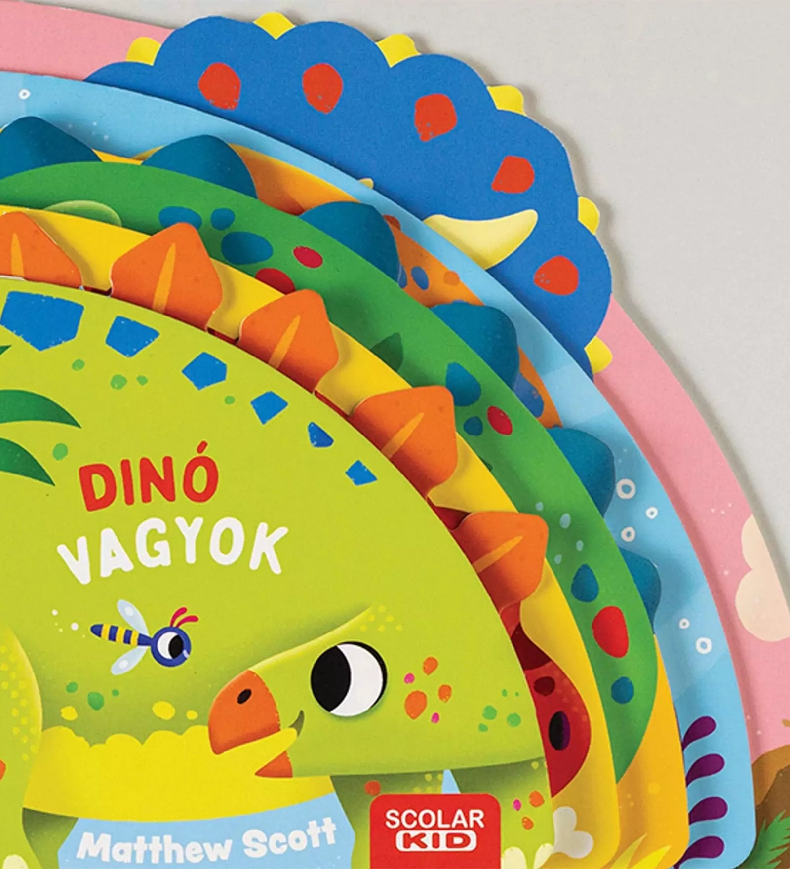  Színes, félkör alakú, magyar nyelvű gyerekkönyv borítója „Dinó vagyok” címmel, különböző dinoszauruszok fejeit ábrázoló oldalrétegekkel, Scolar KID kiadásban.