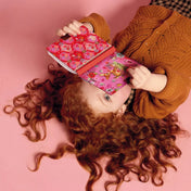 Egy vörös hajú kislány rózsaszín háttéren fekve lapozza a Fiona titkos naplóját. A napló fedelén az őzike, virágok és madarak színes illusztrációi láthatók, játékos, mesés hangulatot teremtve.