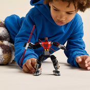 Egy kisfiú figyelmesen játszik a teljesen megépített Darth Maul mecha figurával, amely vörös fénykardot tart a kezében.