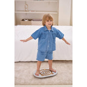 Kisgyermek karjait kitárva egyensúlyozik a Viga egyensúlyozó és koordinációs táblán a szobában.