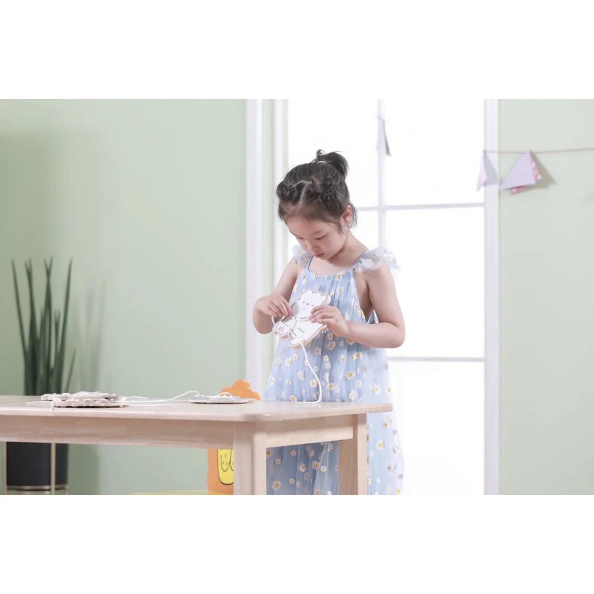 Kislány a PolarB Viga „Fűzd össze az állatokat” készlettel játszik, egy állatfigurát fűz át zsinórral egy asztal mellett.