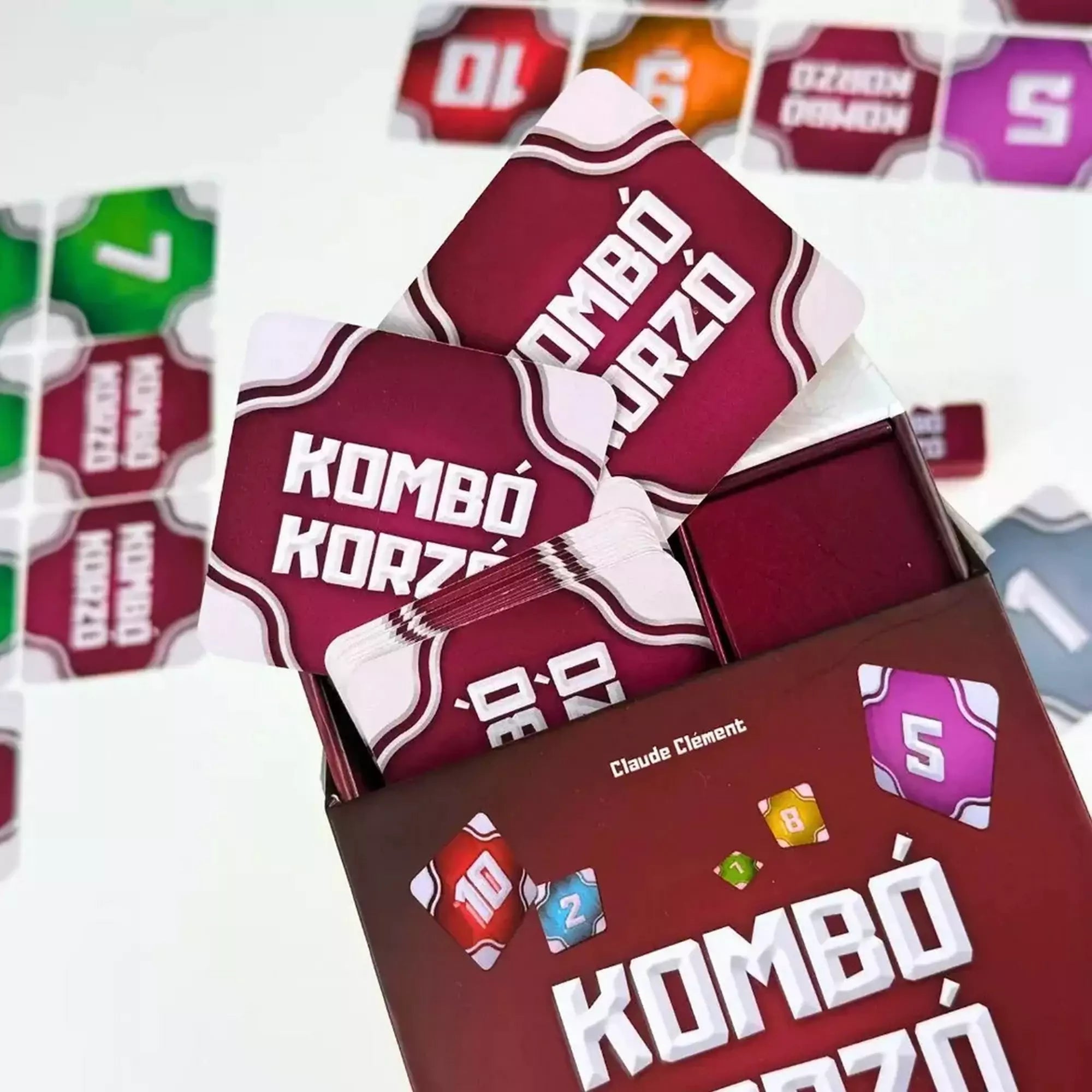 A Kombó Korzó társasjáték dobozából kilógó paklik, piros hátlapú kártyák és a háttérben színes lapok láthatók.