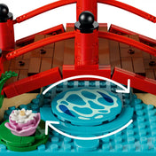 Közeli részlet a LEGO Animal Crossing: Timmy és Tommy vidám kirándulása 77059 készlet forgatható taváról, amely mozgásba hozva azt az illúziót kelti, mintha a halak a vízben úsznának a piros híd alatt.