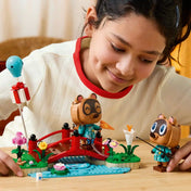 Egy gyermek a LEGO Animal Crossing: Timmy és Tommy vidám kirándulása 77059 készlettel játszik, miközben Timmy és Tommy figurái a piros hídon horgásznak, ajándékot emelnek a magasba és felfedezik a tópartot.