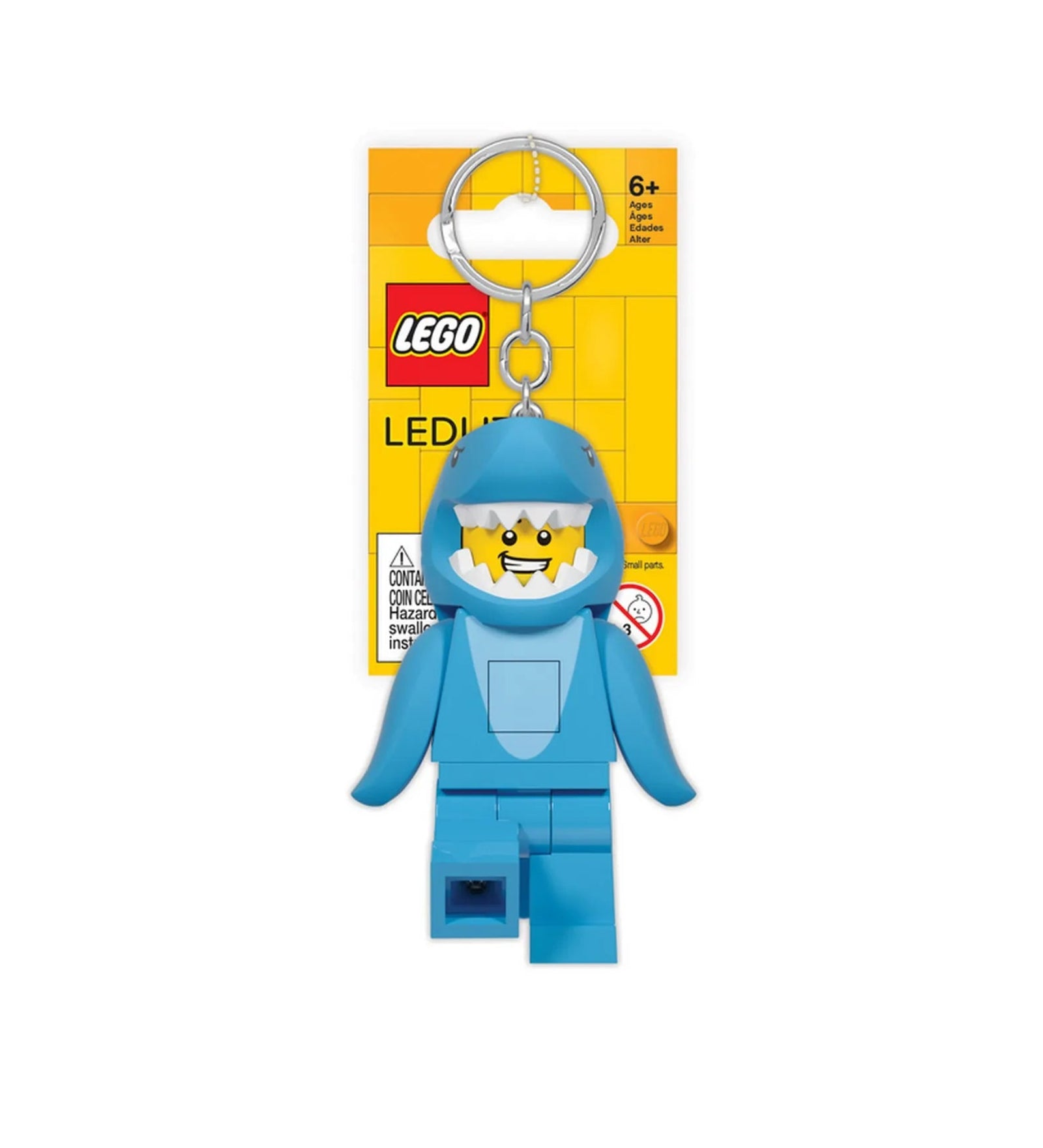 A képen a LEGO LED Shark Guy kulcstartó látható, kék cálarcú minifigura formájában, sárga LEGO háttérlapos csomagolásban. A figura vidáman mosolyog, és a kulcstartó tetején ezüstszínű fémkarika található.