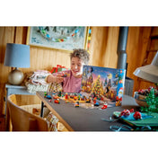 Egy mosolygó gyermek a LEGO City: Adventi naptár 2026, 60510 készlet karácsonyi figuráival játszik az asztalnál.