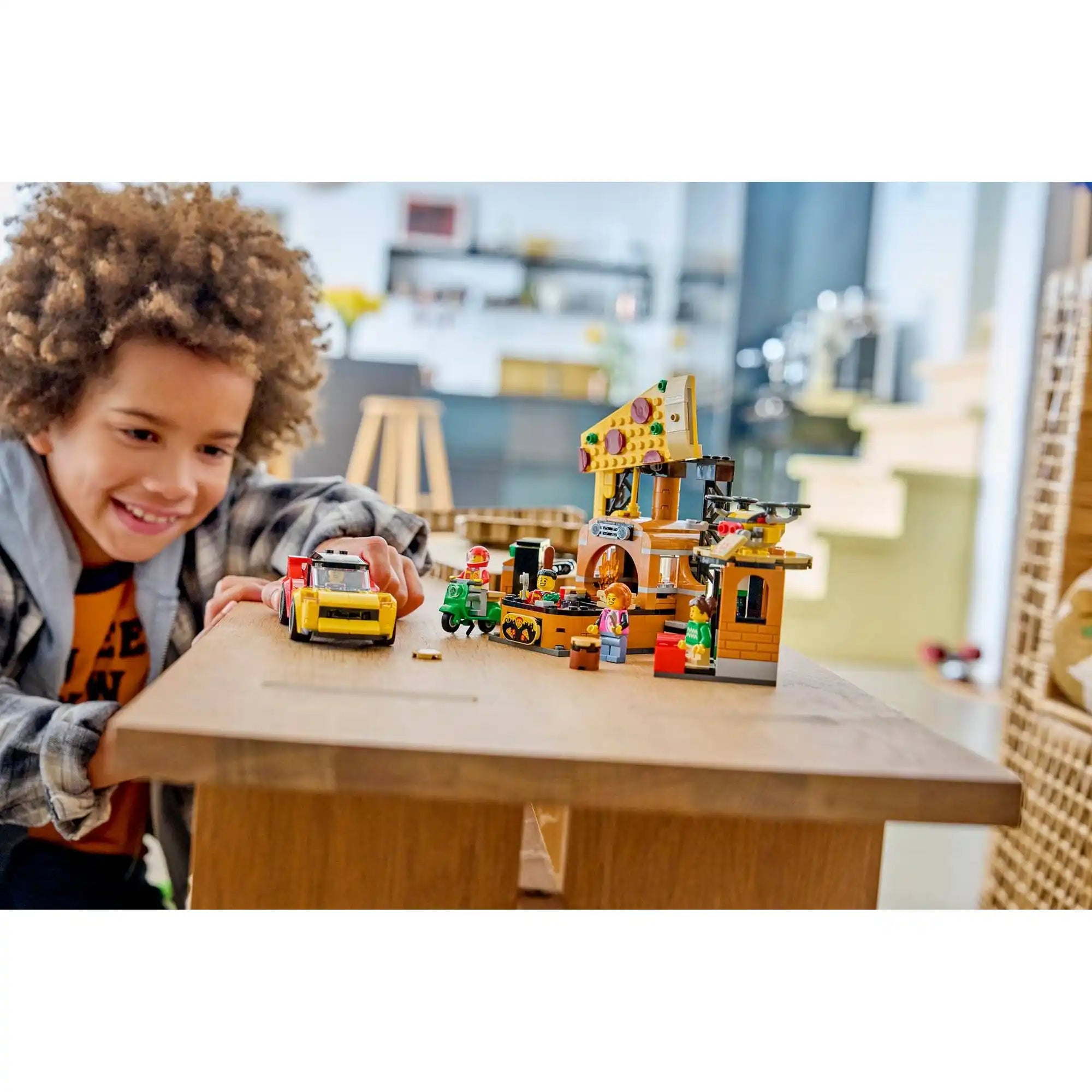 Gyermek játszik a LEGO City 60496 pizzériával, miközben a pizzakiszállító autót és az étterem elemeit használja.