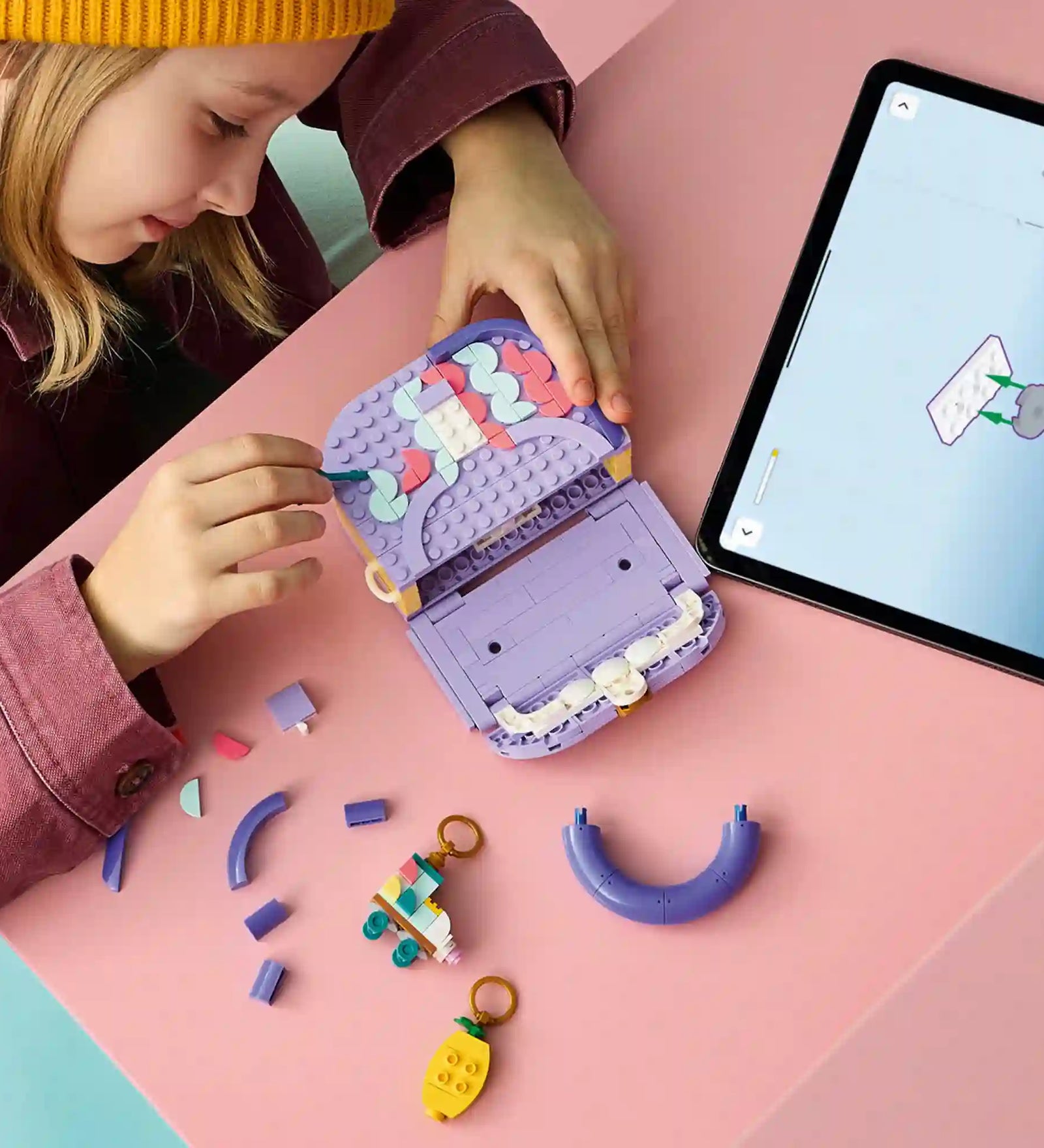Gyermek építi és testre szabja a LEGO Creator Dekorálható táska modellt, miközben a LEGO Builder alkalmazás digitális útmutatóját használja egy tableten.