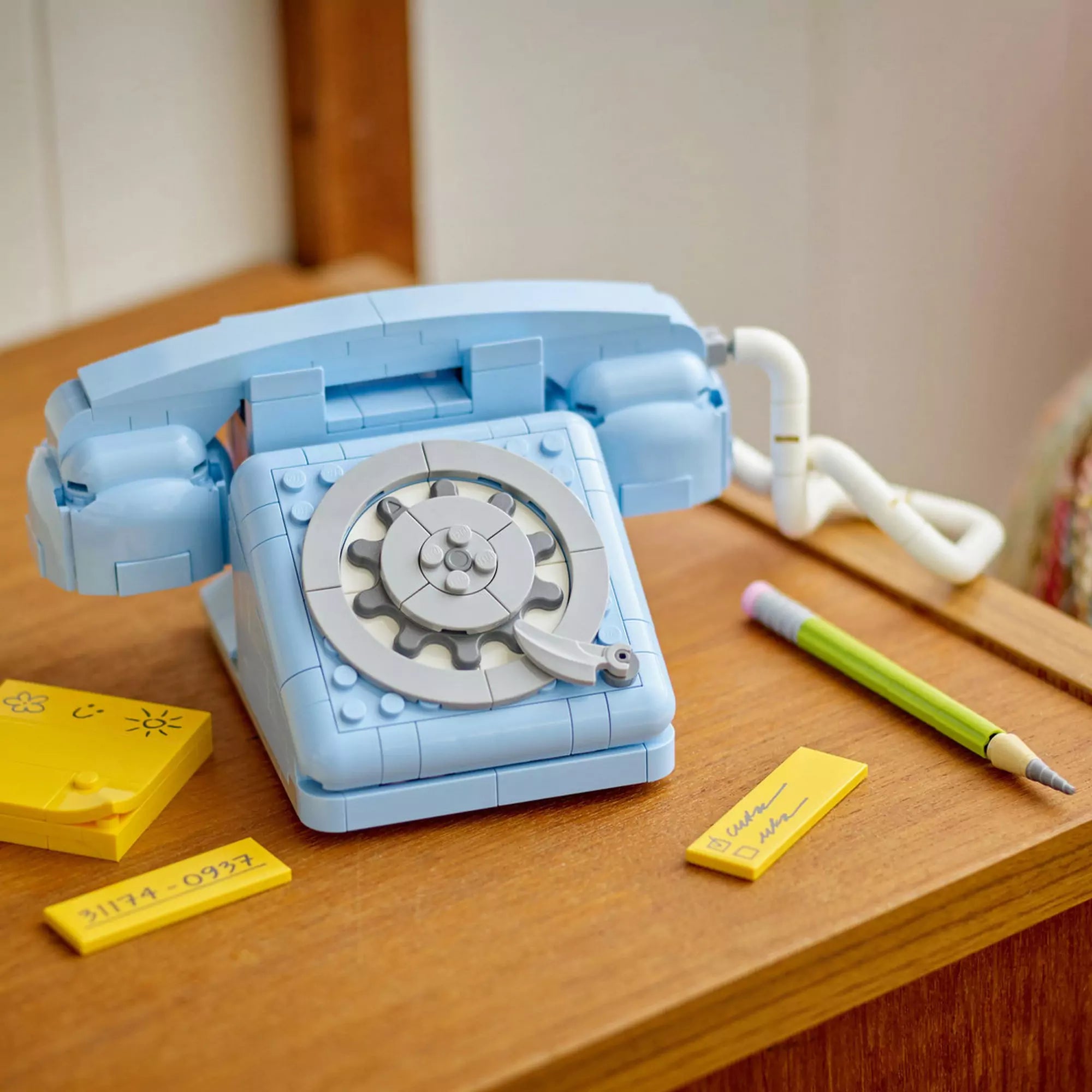 A LEGO Creator Retro telefon (31174) világoskék tárcsás modellje egy faasztalon, mellette sárga jegyzettömb és LEGO ceruza.