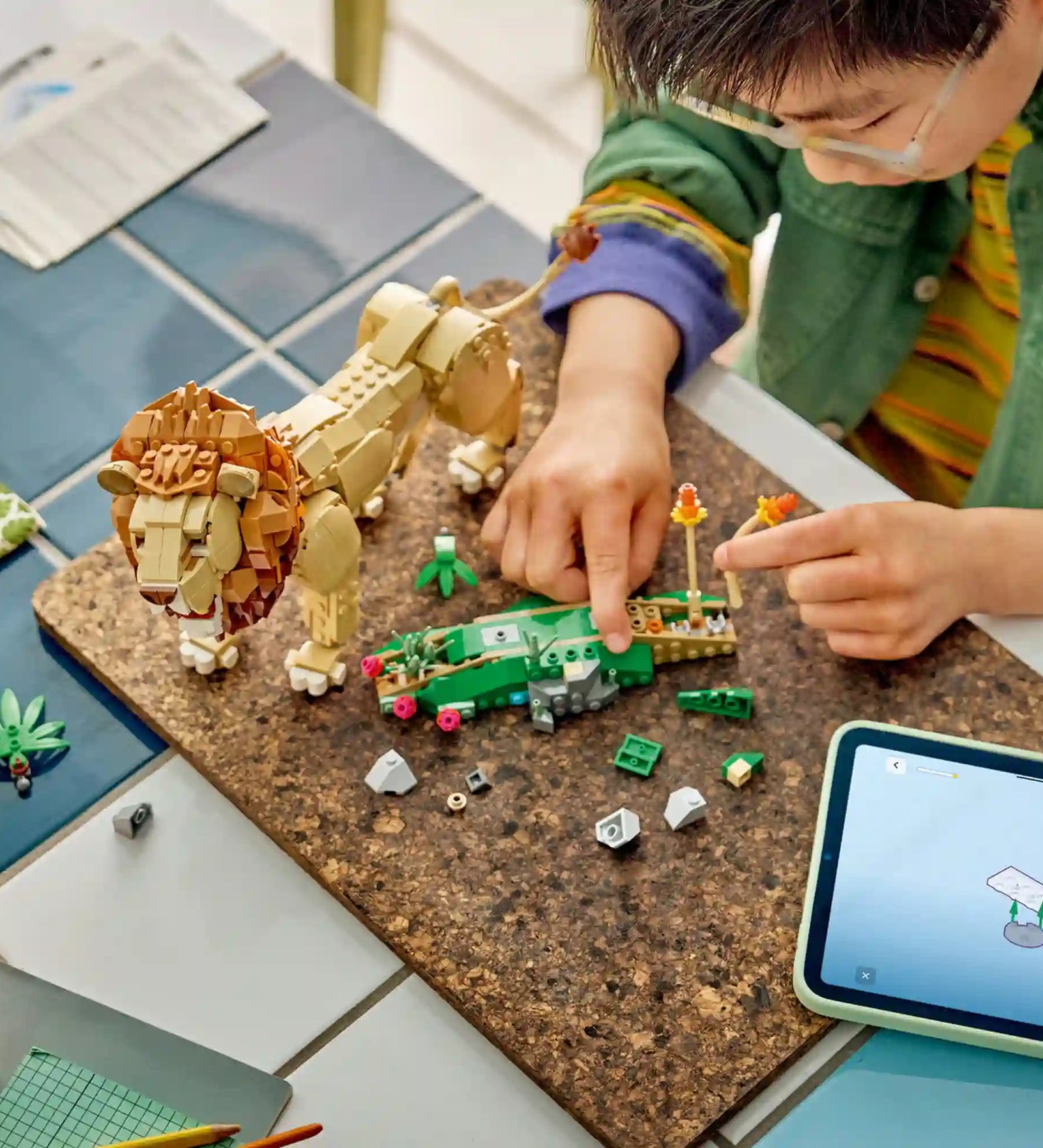 Gyermek építi a LEGO Creator Vadállatok: Fenséges oroszlán (31386) készletet egy asztalon.