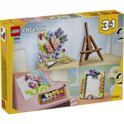 LEGO Creator 3 az 1-ben Virágos műalkotás (31390) készlet hátoldali dobozképe, amely bemutatja a megépíthető virágos faliképet rózsaszín pillangóval, kék virágokkal és lila bogyókkal, valamint a készlet alternatív építési lehetőségeit, köztük egy díszes képkeretet és festőállványos kiállítást.