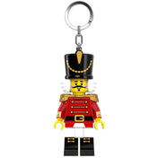 A LEGO Diótörő minifigura alakú kulcstartó elölről látható, piros díszruhában, fekete magas sapkával és arany vállpántokkal.