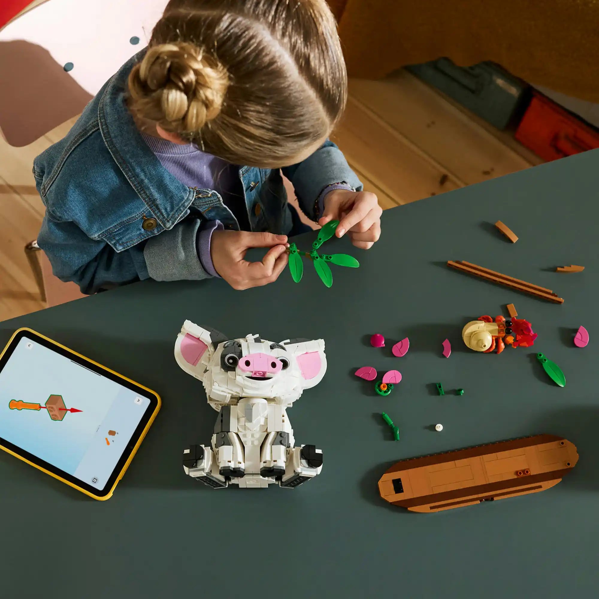 LEGO Disney: Pua 43292, 885 darabos készlet építése közben, ahol egy gyermek a pálmaleveles díszítőelemeket szereli össze a LEGO Builder alkalmazás útmutatásával.