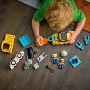 Felülnézetből fotózott LEGO DUPLO építőipari jármű alkatrészek, kisgyermek játék közben szereli össze a sárga rakodógépet és kiegészítőit.