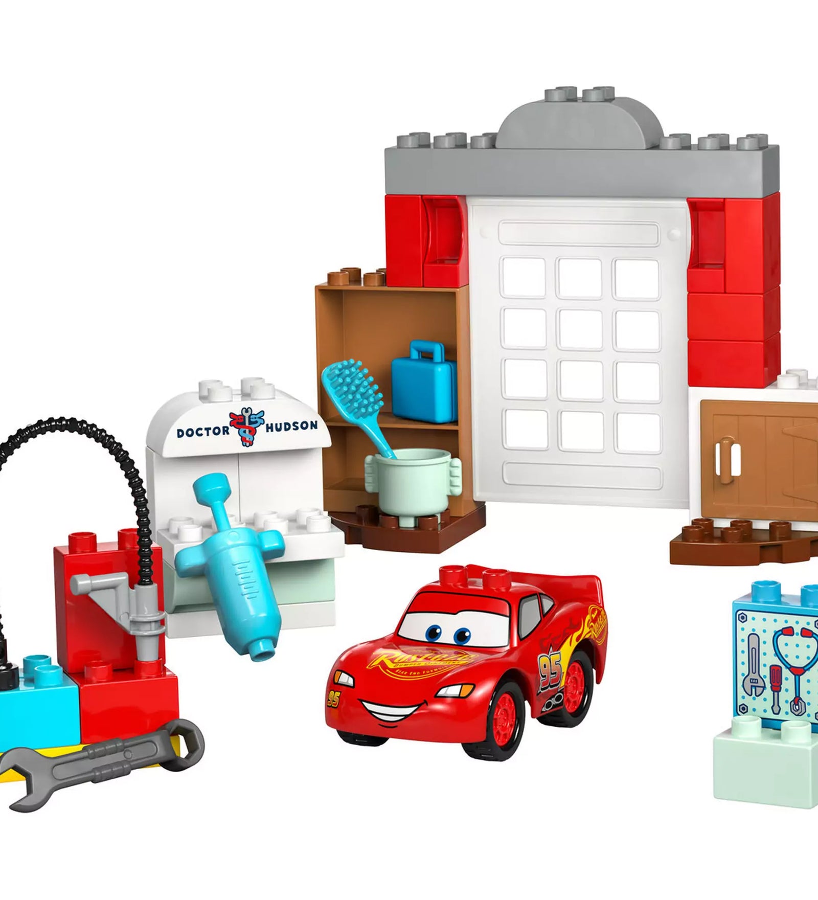A LEGO DUPLO McQueen látogatása Doc garázsában (10456) összes fő eleme elrendezve: garázsajtó, eszközök, Doc Hudson rendelője, és Villám McQueen figura.