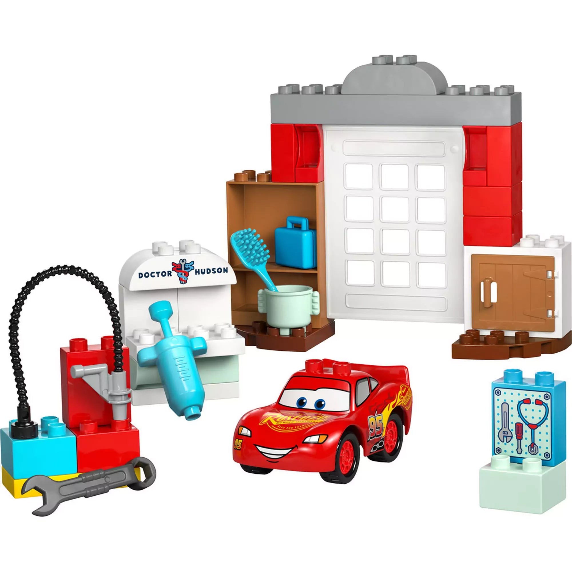 A LEGO DUPLO McQueen látogatása Doc garázsában (10456) összes fő eleme elrendezve: garázsajtó, eszközök, Doc Hudson rendelője, és Villám McQueen figura.