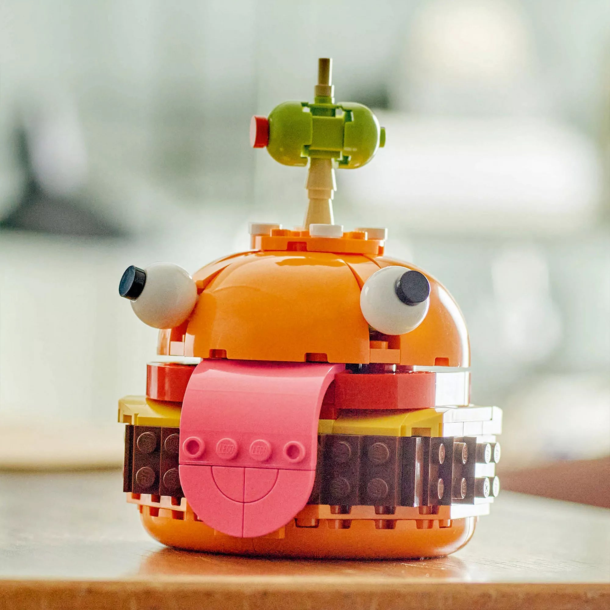Közelkép a LEGO Fortnite Durrr Burger modellről, amelyen láthatóak a részletes elemek: a kinyújtott rózsaszín nyelv, a mozgatható szemek és az olíva a tetején, fogpiszkálón rögzítve.