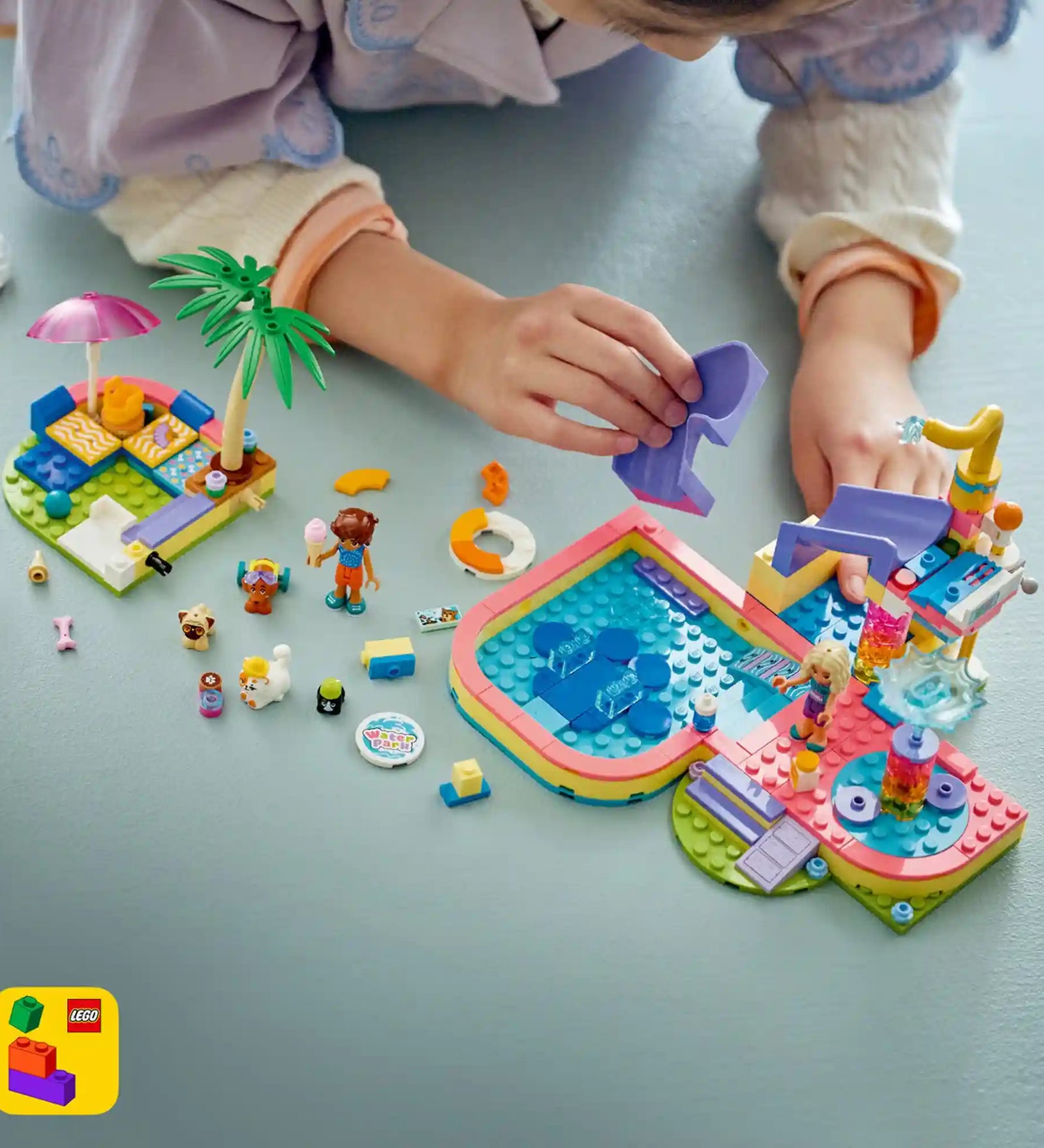 Gyermek a LEGO Friends 42676 aquapark készlettel játszik, miközben a házi kedvencek a csúszdán és a medencében szórakoznak.
