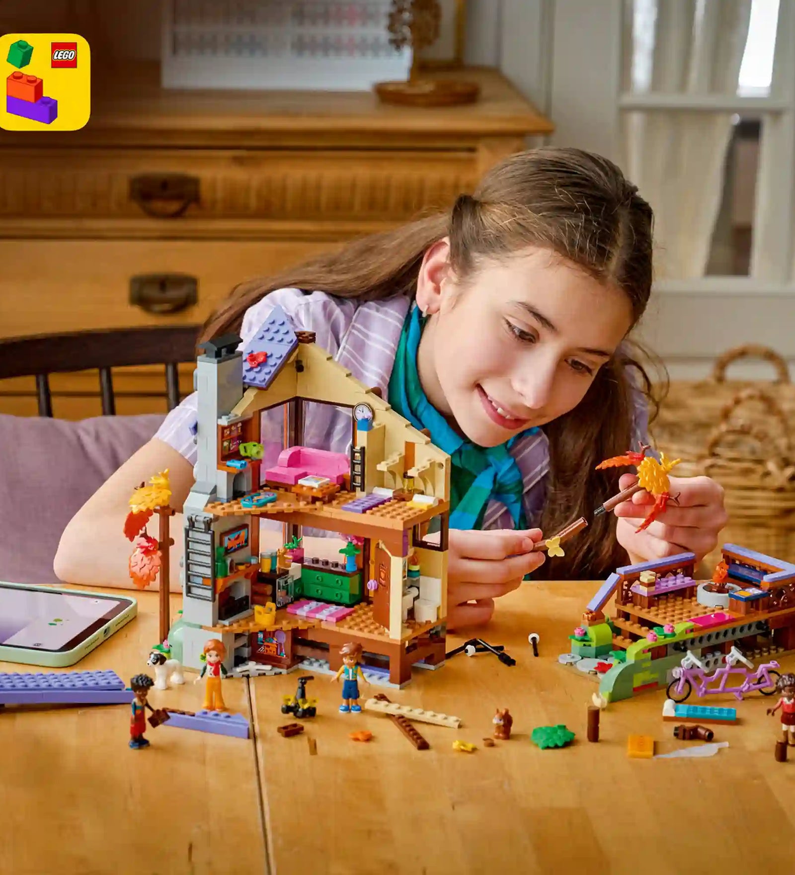 Gyermek építi a LEGO Friends erdei kabint, miközben a LEGO Builder alkalmazás digitális 3D-s építési útmutatóját használja.
