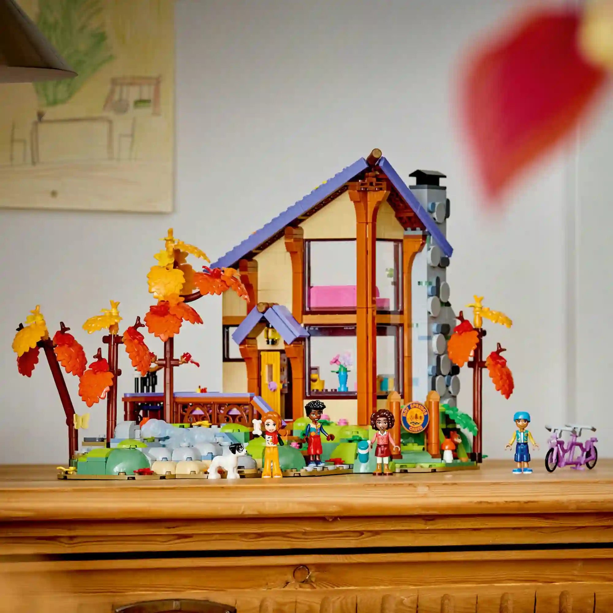 LEGO Friends Otthonos kabin az őszi erdőben teljes modellje egy bútoron kiállítva, színes lombkoronás fákkal, patakkal és Friends figurákkal.