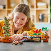 Mosolygó gyermek játszik a LEGO Harry Potter Roxforti gyógynövénytan növényei (76474) készlettel. Az előtérben a Mimbulus mimbletonia növény, a harapós muskátlik és a mandragóra modell látható a Roxfort gyógynövénytan óráit idéző hangulatban.