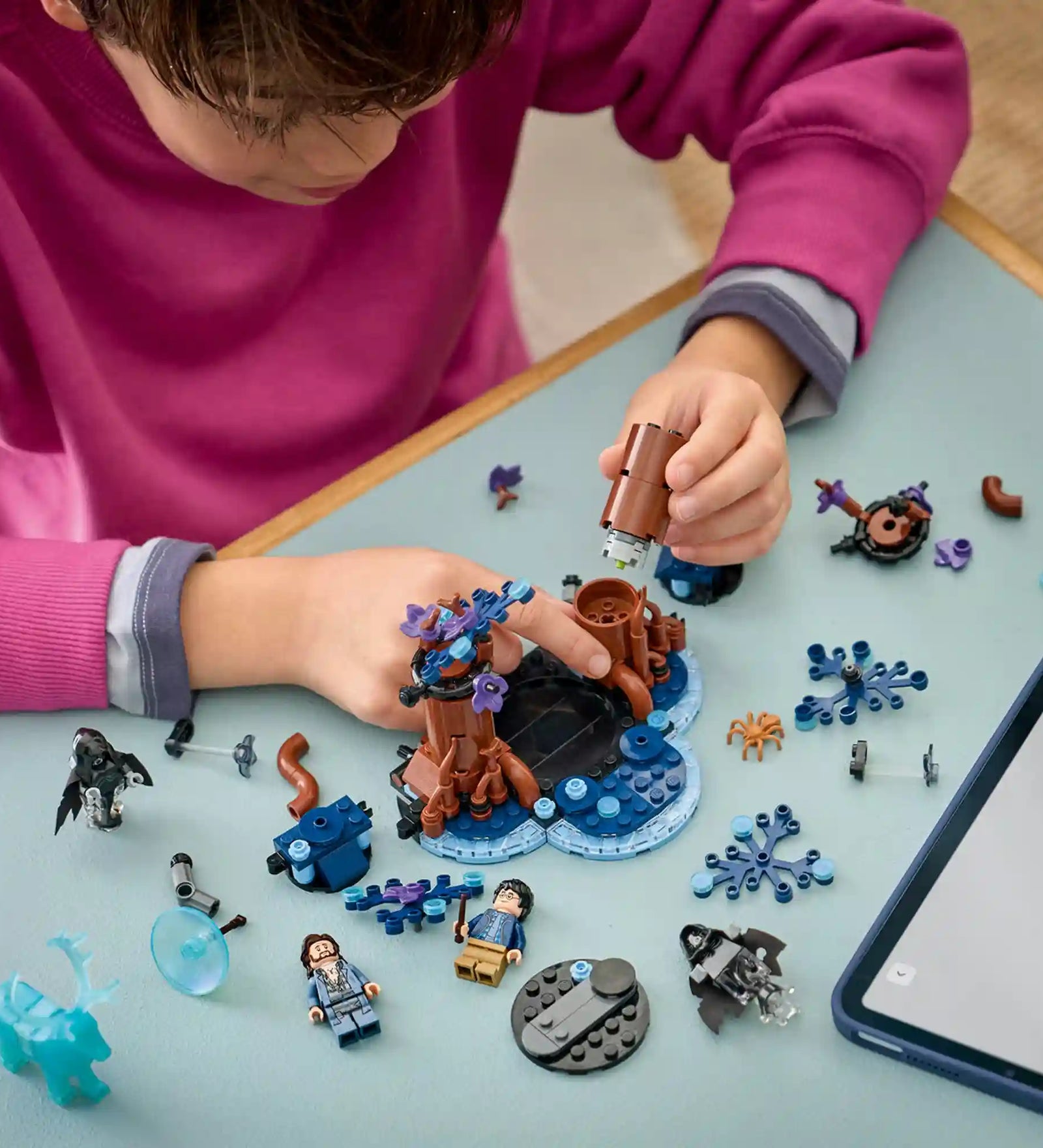Gyermek építi a LEGO Harry Potter A Tiltott Rengeteg: Expecto Patronum készletet, miközben a LEGO Builder alkalmazás digitális útmutatóját használja.