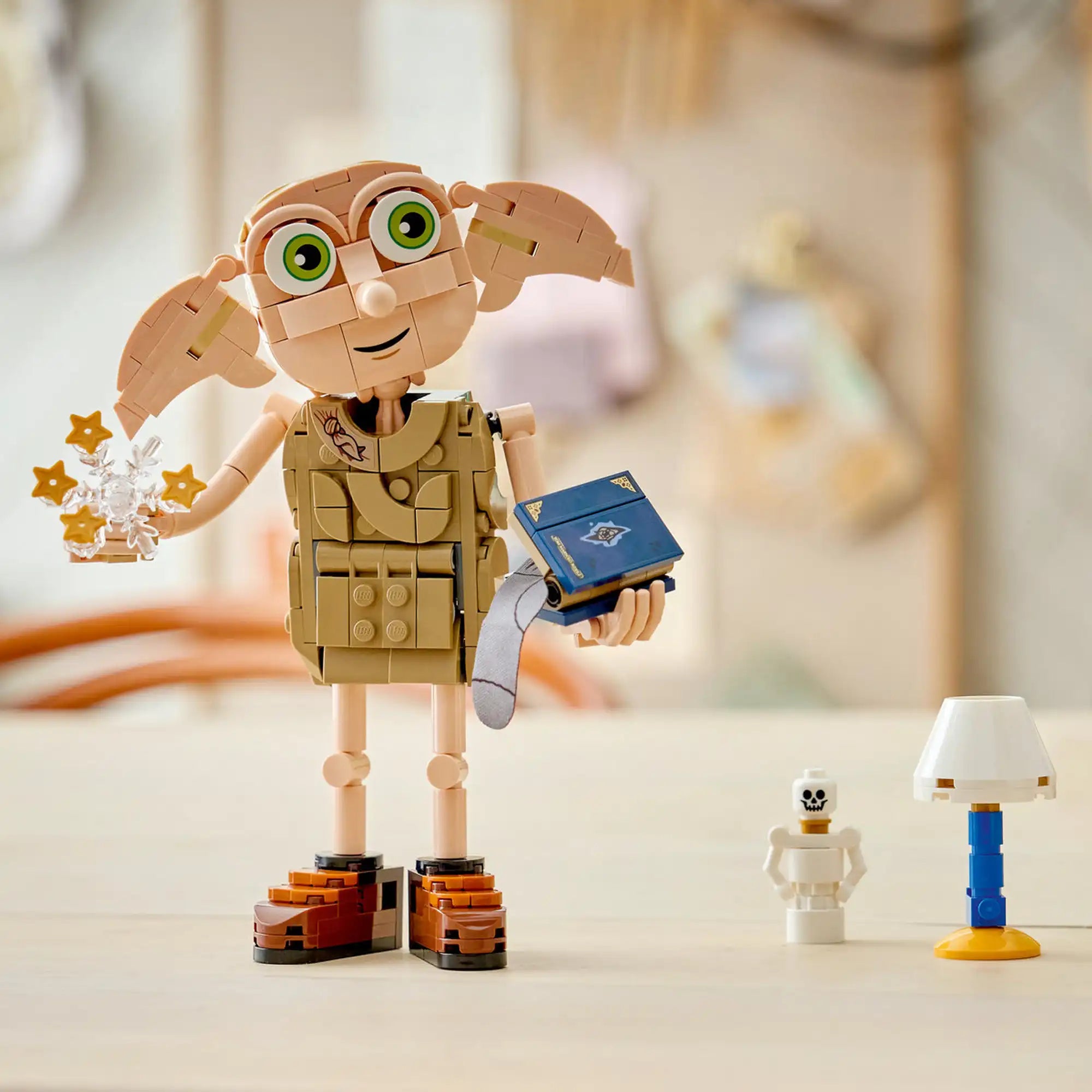 LEGO Harry Potter Dobby™ a házimanó 76469 megépített figura életképben, mozgatható fejjel és fülekkel, kezében Tom Denem naplójával és varázslatos tortadísz elemmel, mellette Hedwig emléktárgy és lámpa.