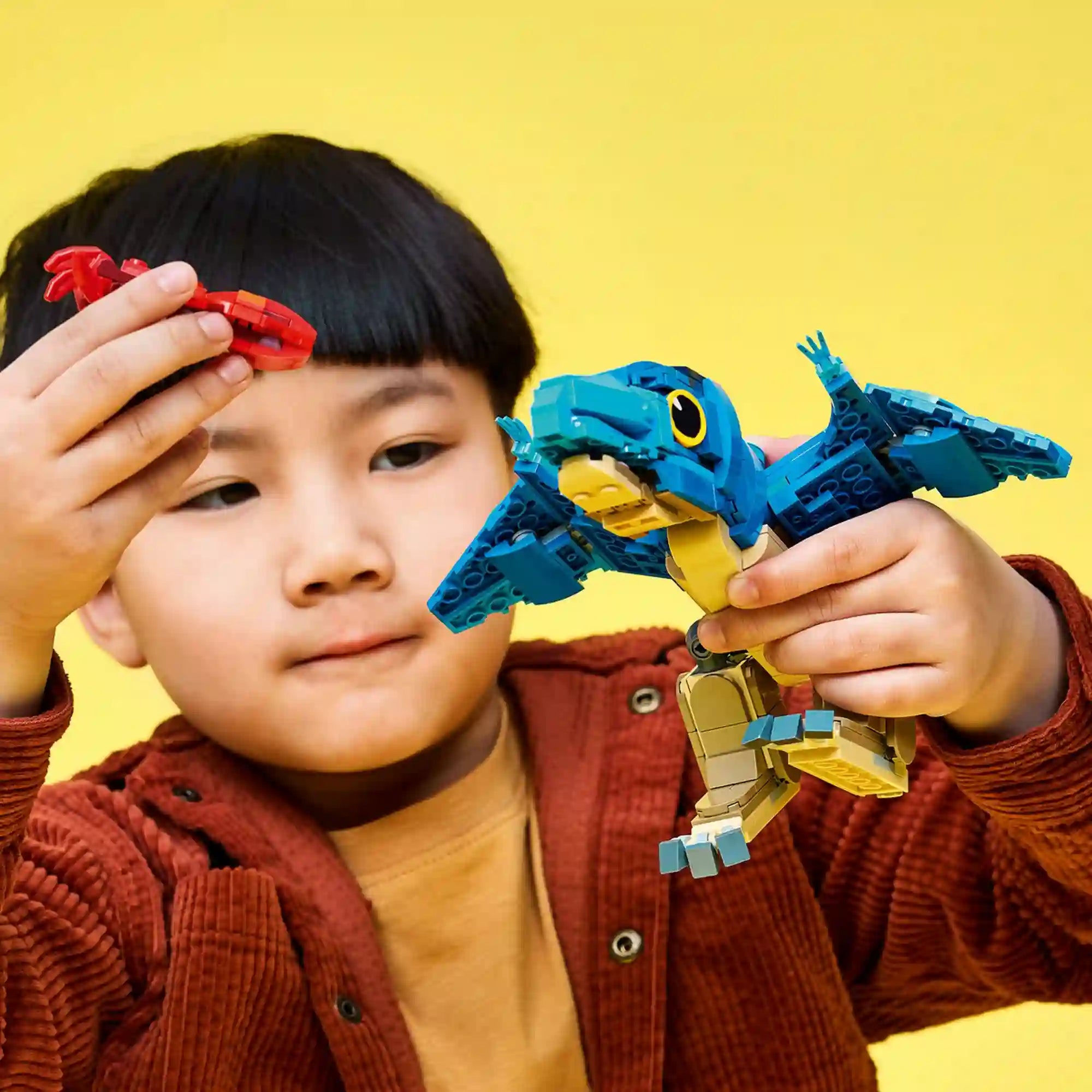 Gyermek játék közben: Kisfiú a LEGO Jurassic World Bébi pteranodon figurával játszik, miközben a piros tintahal kiegészítőt tartja a kezében.