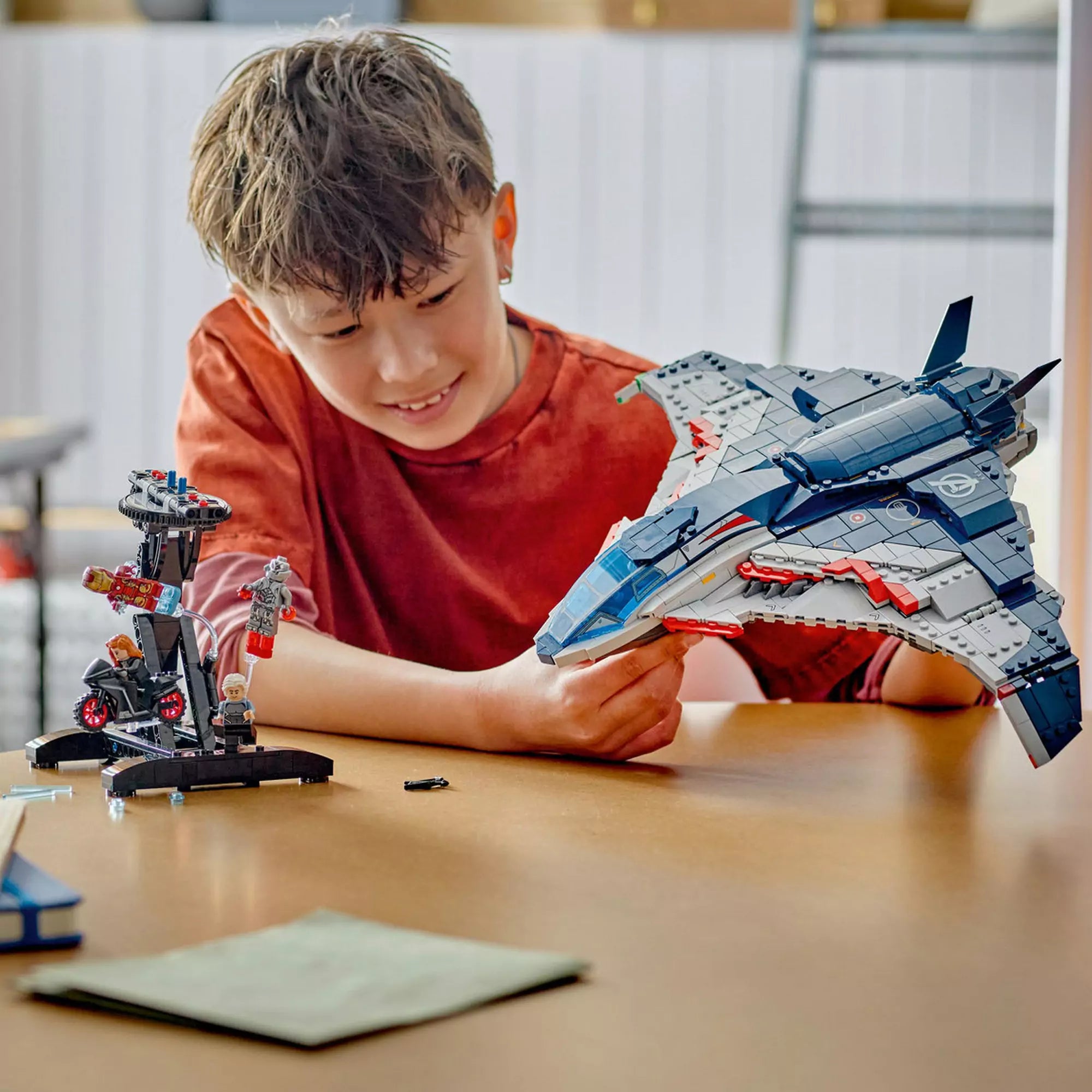 Fiú játszik a LEGO Marvel Quinjet (76325) készlettel, kézben tartva a repülőt, mellette az akciójelenetet bemutató állvány.