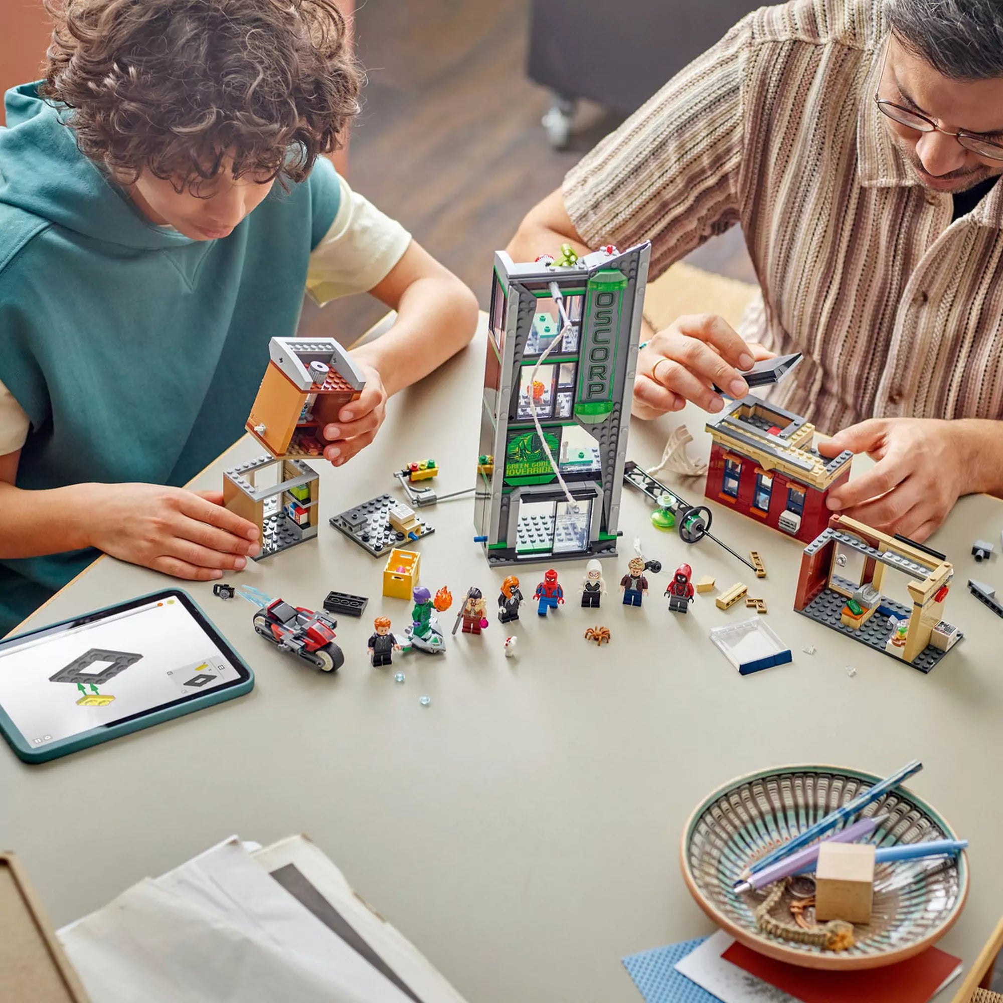 LEGO Marvel Pókember vs. Oscorp (76324) építése asztalon, figurákkal és tabletes útmutatóval.