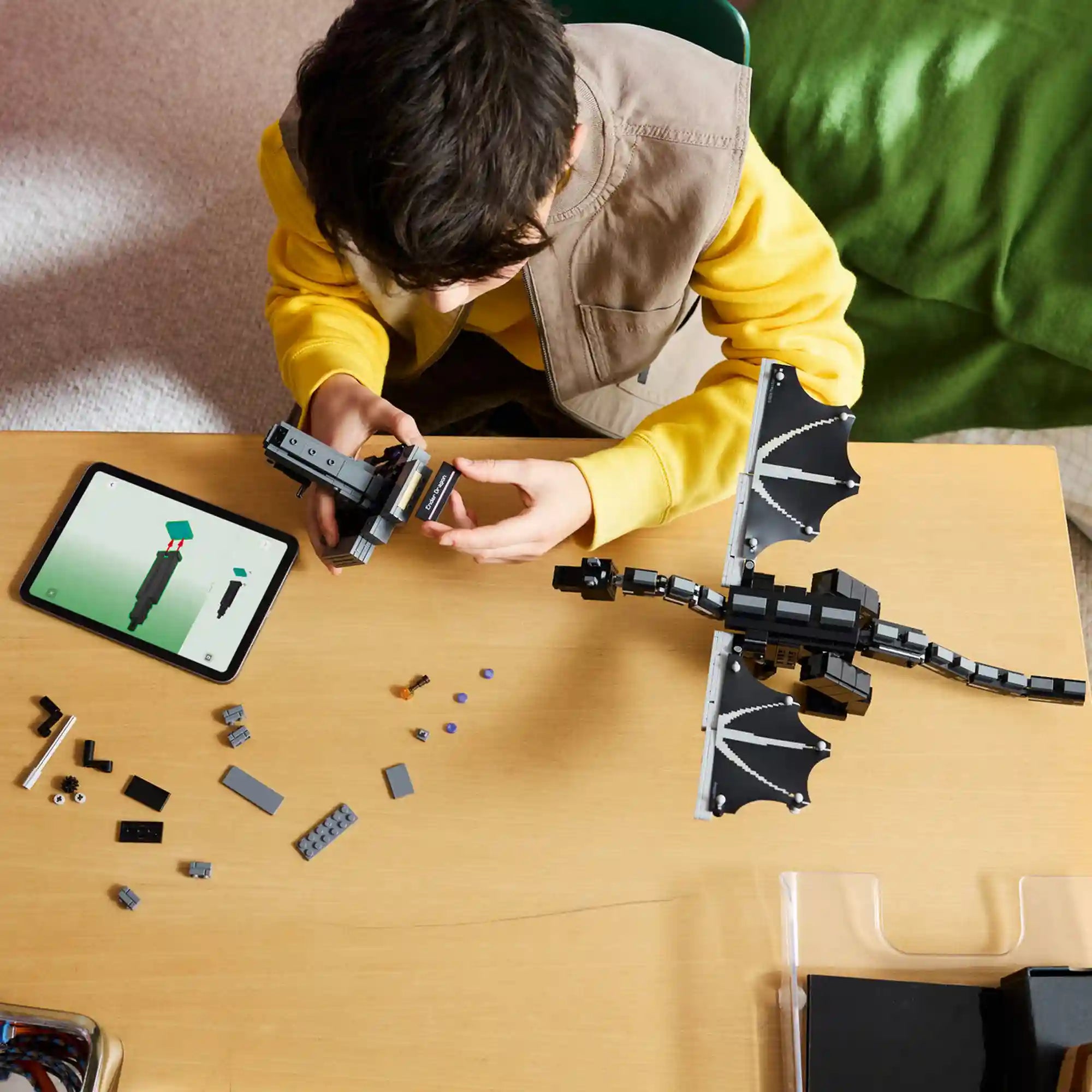 Gyermek építi a LEGO Minecraft Végzetsárkány (21595) modellt, miközben egy táblagépen a LEGO Builder alkalmazás 3D-s útmutatója segíti az összeszerelést.