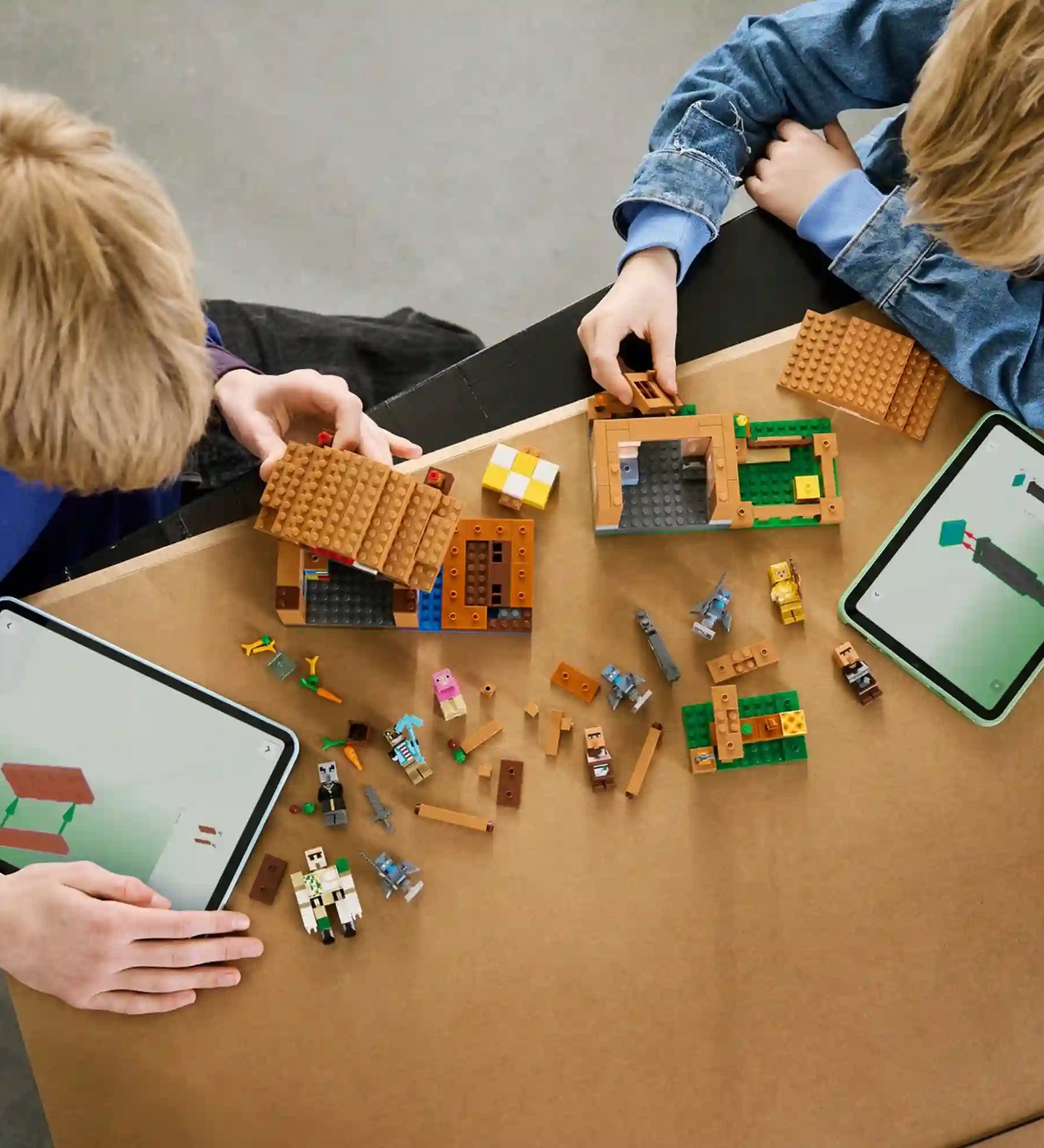 Két gyermek építi a LEGO Minecraft Idézőtámadás a faluban 21596 készletet, miközben tableten követik a LEGO Builder digitális útmutatóját.