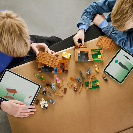 Két gyermek építi a LEGO Minecraft Idézőtámadás a faluban 21596 készletet, miközben tableten követik a LEGO Builder digitális útmutatóját.