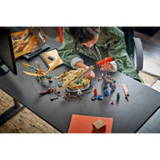 Gyermek a LEGO NINJAGO Összecsapás a Sárkány Kardjánál 71871 készletet építi, miközben a sárkány, az Oni robot és a minifigurák az asztalon láthatók.