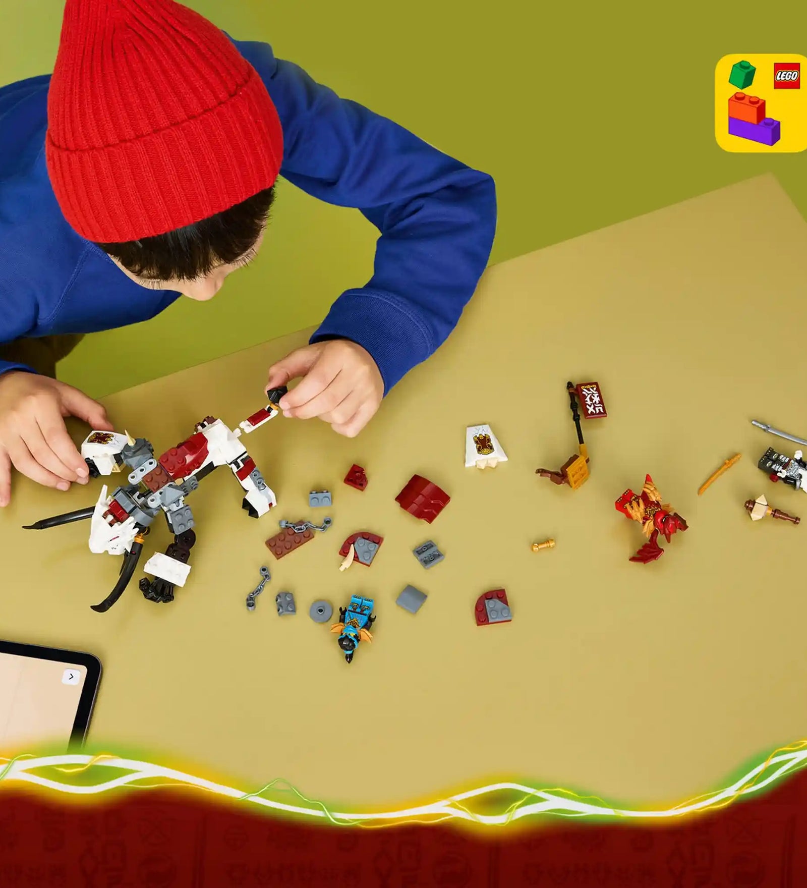 Gyermek a LEGO Builder alkalmazás segítségével építi a LEGO NINJAGO 71863 Grimtak sárkányszörny készletet, az elemek és figurák az asztalon láthatók.