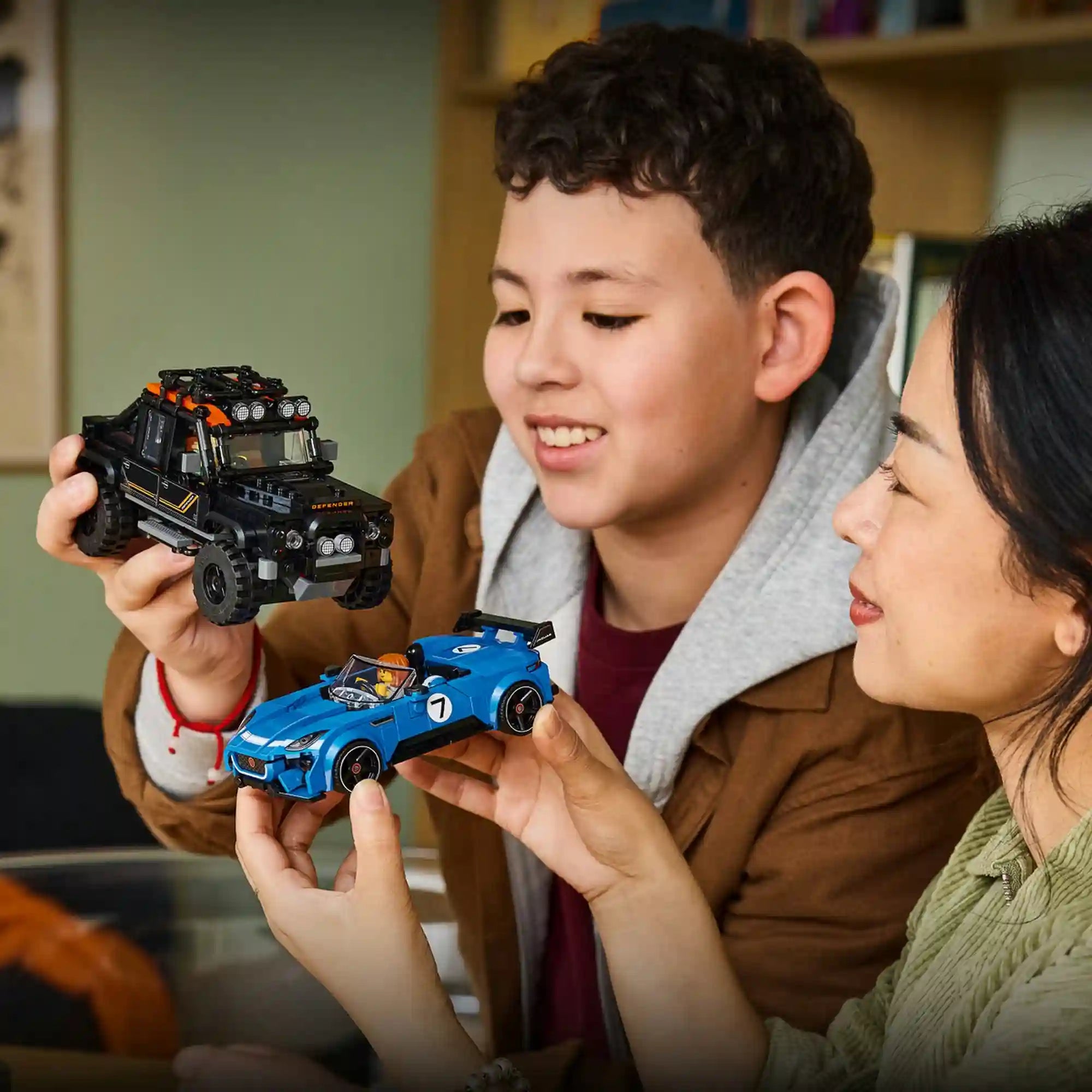 Modellek kézben: Gyermek és felnőtt kézben tartja a LEGO Jaguar Project 7 sportautót és a Land Rover Defender Classic terepjárót.