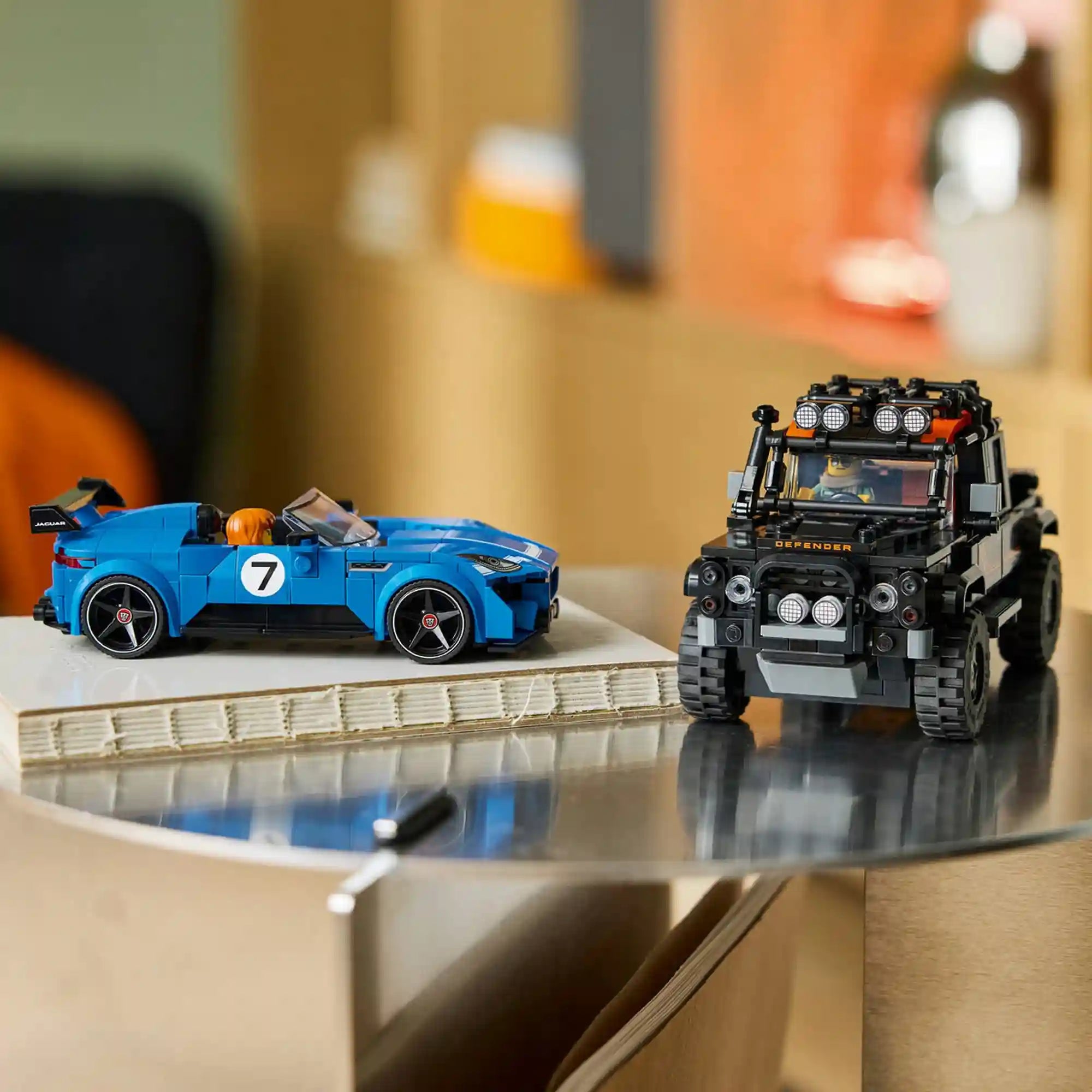 Kiállított autók: LEGO Jaguar Project 7 és Land Rover Defender Classic modellek kiállítva egy asztalon modern enteriőrben.