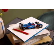 A LEGO Speed Champions Visa Cash App RB VCARB 01 F1 versenyautó 77246 kiállítva könyveken, piros tollal mellette.