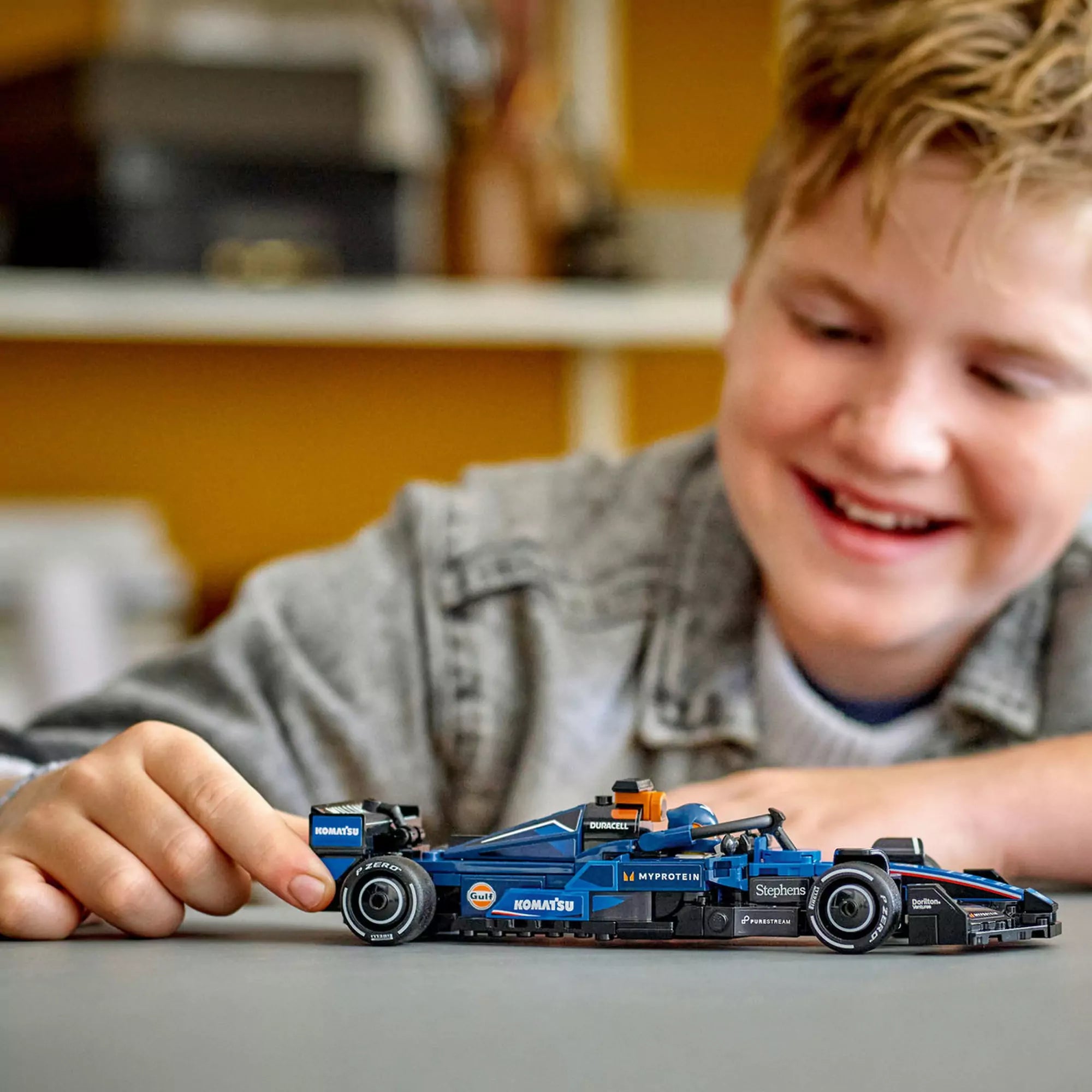 Kisfiú mosolyogva tologatja az elkészült LEGO Williams FW46 autót egy asztalon, játék közben