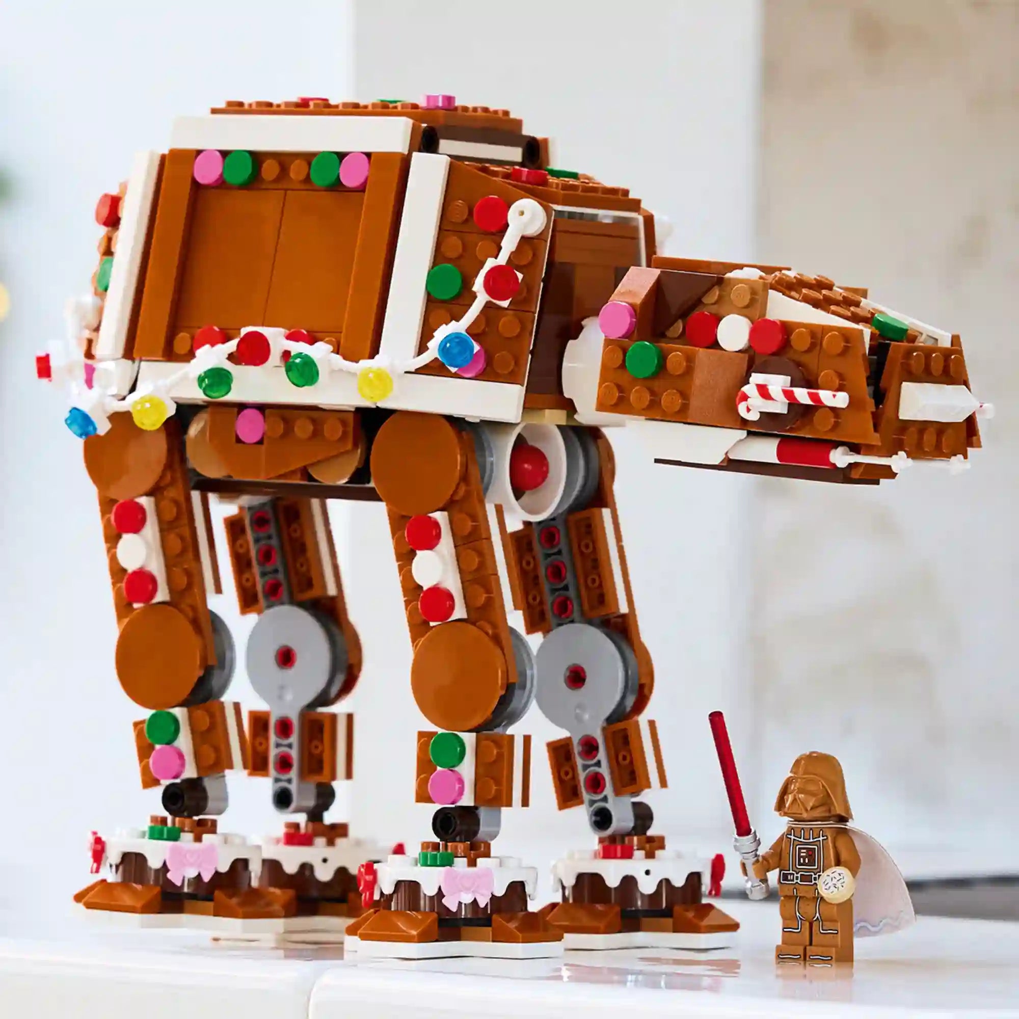 LEGO Star Wars: Mézeskalács AT-AT lépegető 40806 barna modellje színes cukorkadíszekkel, fényfüzérrel és Darth Vader figurával.