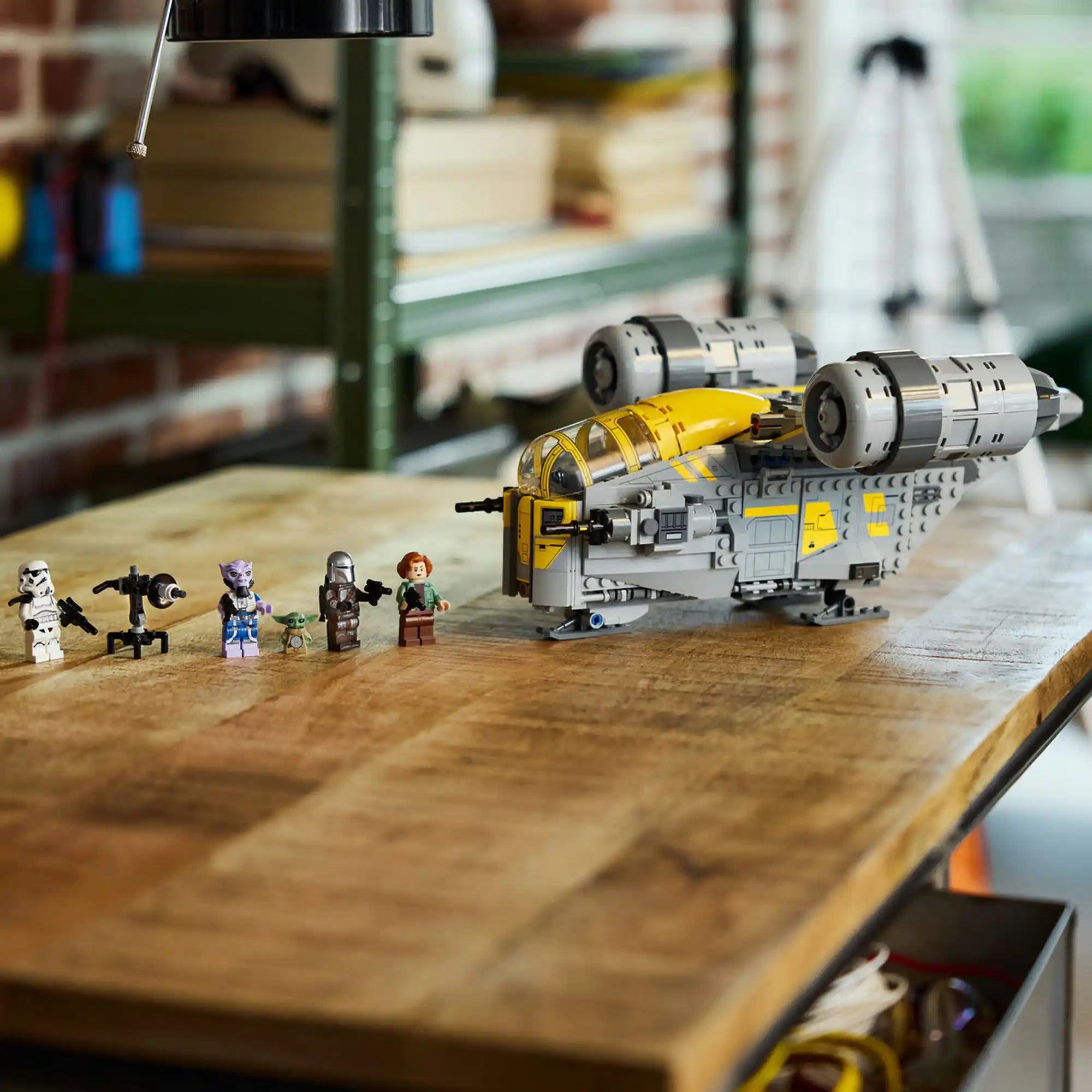 LEGO Star Wars 75447 The Razor Crest űrhajó minifigurákkal egy faasztalon, részletes kidolgozású jármű és karakterek sorban mellette.