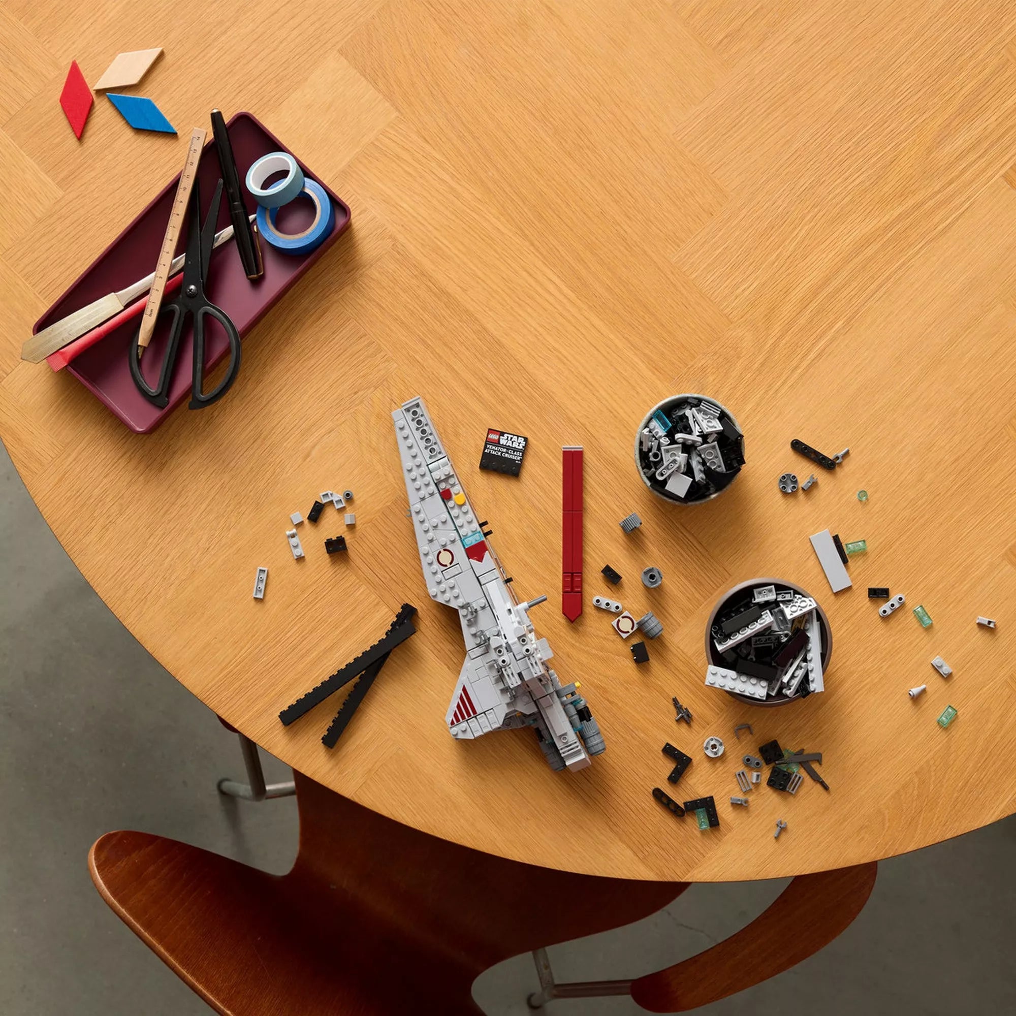 LEGO Star Wars Venator-osztályú támadó cirkáló építőkészlet szétszedett elemei egy faasztalon, külön panelek, talapzat és szerkezeti alkatrészek az építés bemutatására.