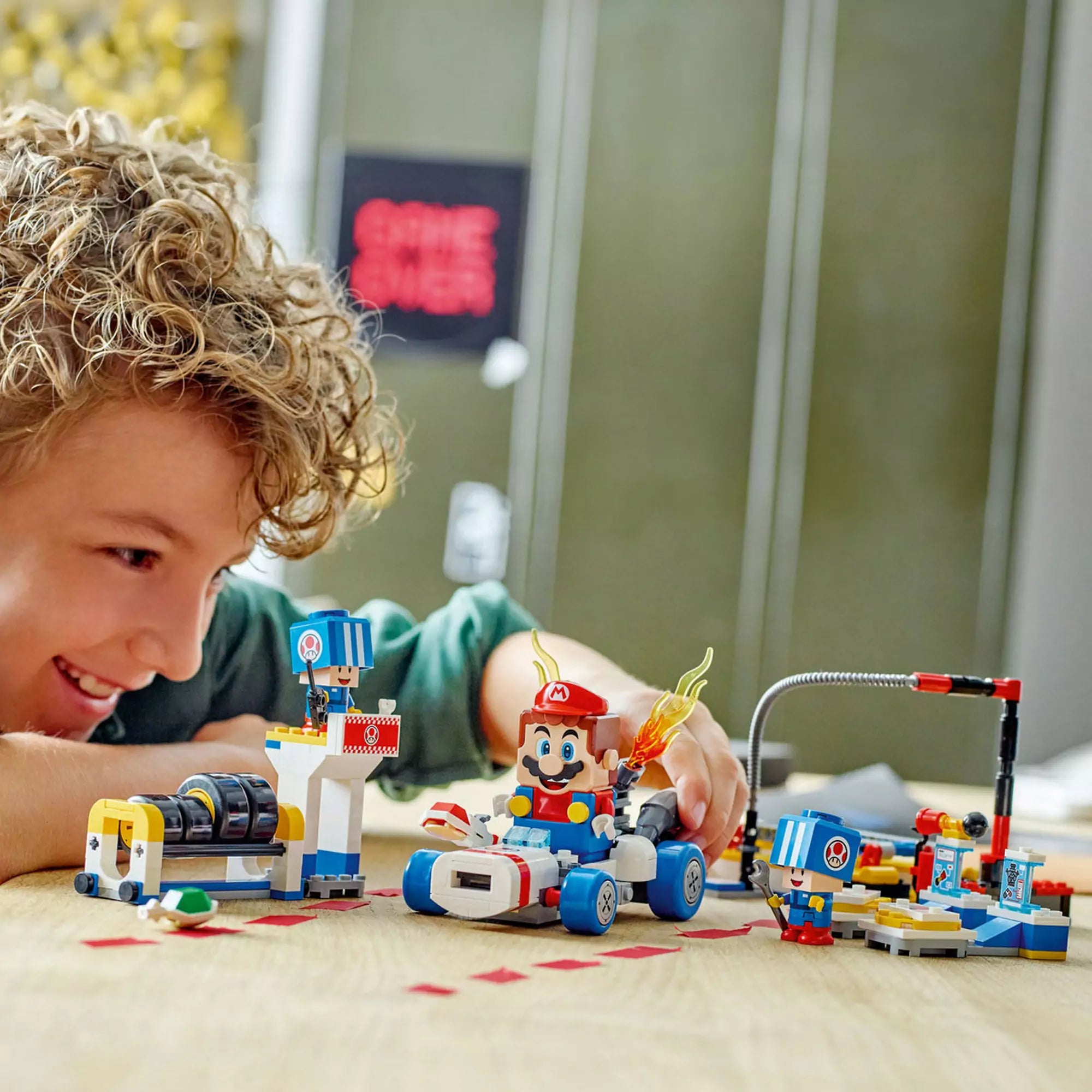  Egy gyerek játszik a LEGO Super Mario Mario Kart, Toad garázsa (72035) készlettel, ahol Mario autóját javítja és felkészíti a versenyre.