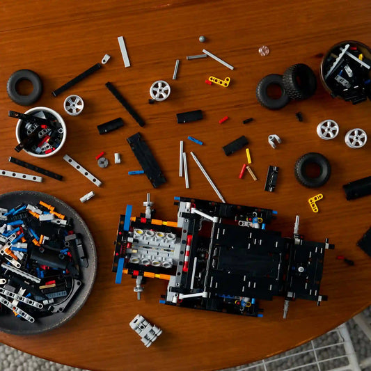 A LEGO Technic 42231 Dodge Charger R/T építési folyamata, alkatrészekkel és részben elkészült alvázzal egy asztalon.